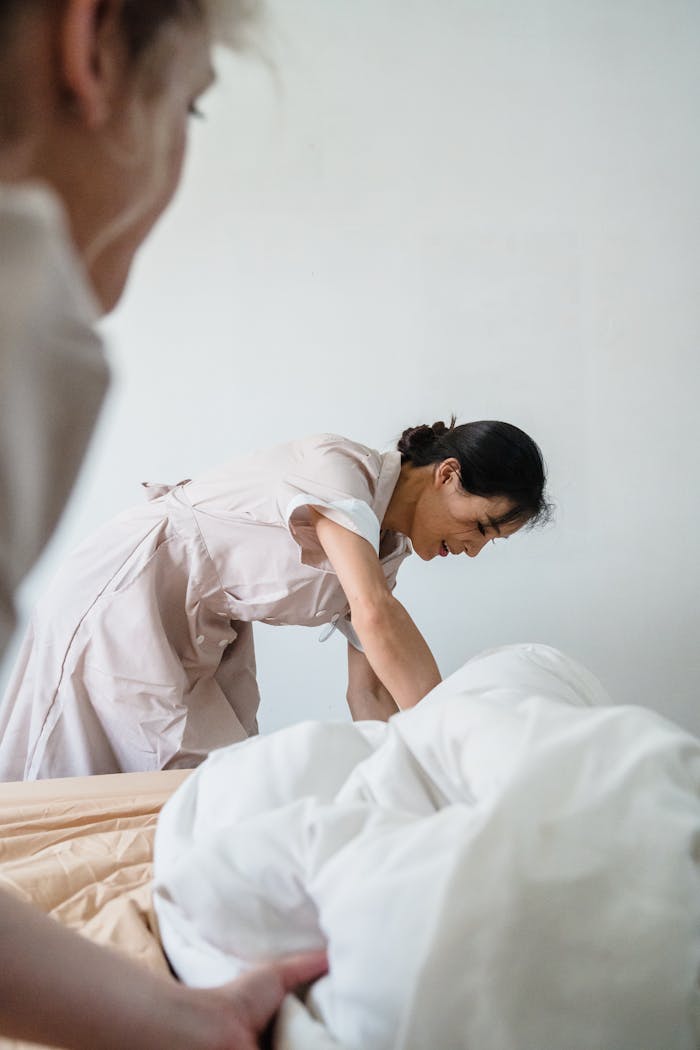 services-04 Housekeeper diligently making a bed with pristine white linens in a hotel room.