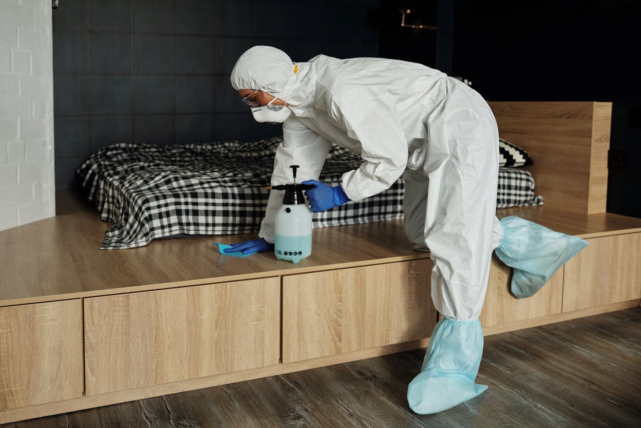 services-01 Worker in protective gear sanitizing a bedroom during the COVID-19 pandemic.